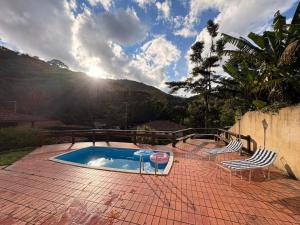 a swimming pool with two chairs and the sun shining at Refúgio Carangola in Petrópolis