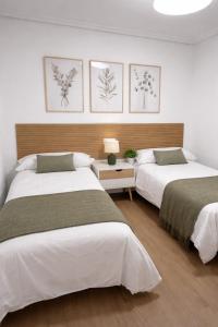 two beds in a white room with paintings on the wall at Entre Plazas in Cáceres