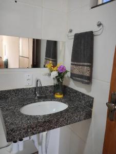 a bathroom counter with a sink and a vase of flowers at Pousada Aconchego in São Mateus