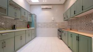 a large kitchen with green cabinets and white tile floors at قو اب إليت in Abā al Kibāsh