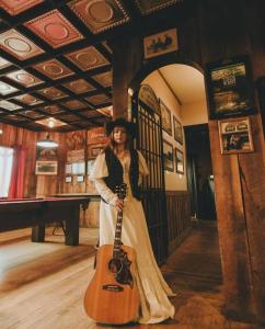 Eine Frau steht in einem Raum und hält eine Gitarre. in der Unterkunft Twin Cities Hotel in Turner Valley
