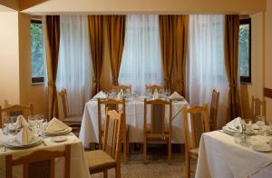 a dining room with white tables and chairs and windows at Pensiunea Floarea de Colt in Nucşoara