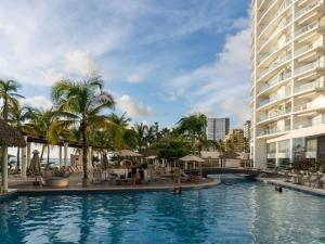 a pool at a resort with palm trees and a building at Luxe Oceanfront Condo in Golden Zone in Mazatlán