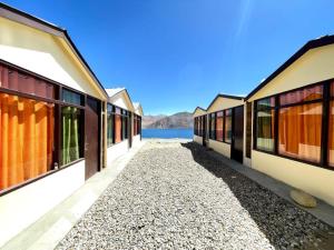 a pathway between two buildings with a lake in the background at zoz camp pangong lake in Lukung