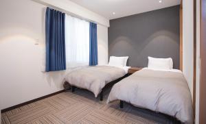 two beds in a room with a window at Shinka Hotel Susukino in Sapporo