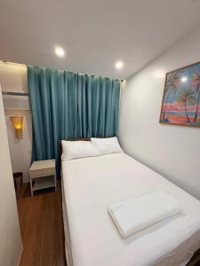 a small bedroom with a white bed with a blue curtain at BMF Tropical Homestay in Calampanan