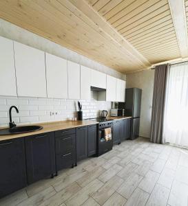 a large kitchen with white cabinets and a wooden ceiling at Котедж HOLIDAY HOUSE in Yablunytsya