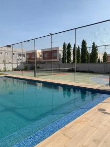 a swimming pool with a tennis court and a fence at Stylish and spacious room in a quiet environment in Dawhwenya