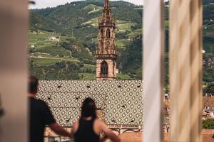 two people looking out of a window at a clock tower at Falkensteiner Hotel Bozen WaltherPark in Bolzano