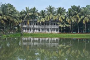 a building with palm trees in front of a body of water at Breathing Earth - Rooms and Pool in Kolkata