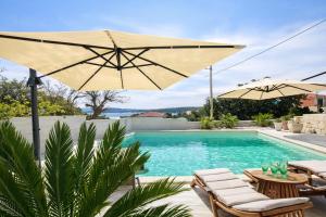a pool with two umbrellas and chairs and a pool at Villa TerraAurora in Barbat na Rabu