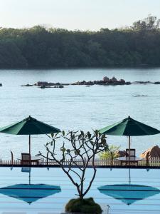 two umbrellas and a tree in front of a body of water at Bay Beach Hotel Nilaveli in Kumpurupiddi