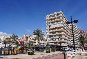 a tall building with palm trees in a city at Hostal Costabella in Fuengirola