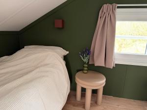 a bedroom with a bed and a stool and a window at De Ree Tiny House Tussen de Dijken in Driewegen