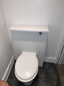 a white toilet with a white shelf above it at M Studio in Raynes Park