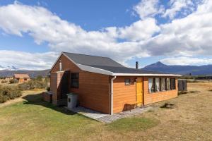 a small house in a field with mountains in the background at Cabañas Lago Tyndall in Torres del Paine