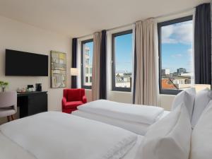 a hotel room with two beds and a red chair at H10 Berlin Ku'Damm in Berlin