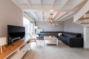 a living room with a black leather couch and a tv at Boszicht 32 in De Haan