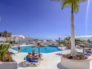 a resort with a pool with people sitting in chairs and a palm tree at Adeje Paradise dreams in Playa Paraiso