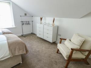 a bedroom with a bed and a chair and a dresser at Hen Siop in Llanfairpwllgwyngyll