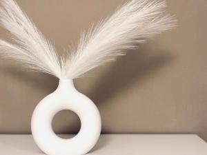 a white vase with a tuft of feathers in it at BorgoLuce Spacious Apt - FREE Parking - Near Airport & Center in Bergamo