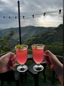 Zwei Personen halten zwei Cocktails auf einem Tisch. in der Unterkunft Ecohotel Java in Manizales