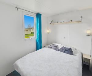 a white bedroom with a bed and a window at Mobilhome in Litteau