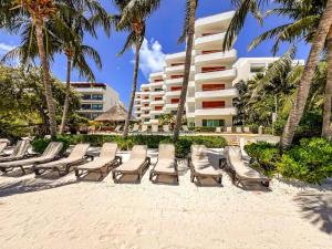 a row of chaise lounge chairs on the beach in front of a hotel at Isla Condo Puerta al Mar 403 at Sac Bajo in Isla Mujeres