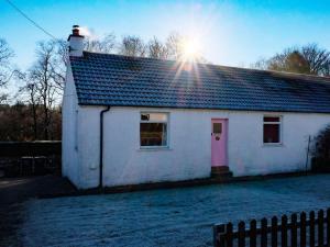 uma casa branca com uma porta rosa e o sol em Culsharg Cottage em Bargrennan