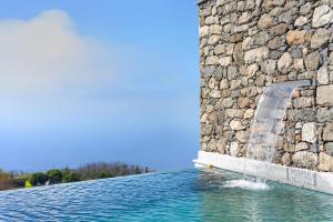 a swimming pool with a stone wall and a water fountain at The Green Valley Porto Moniz in Achadas da Cruz +38 photos
