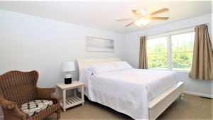 a white bedroom with a bed and a chair at Fairwinds Cottage in Cape May