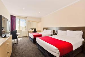 a hotel room with two beds and a flat screen tv at Quality Hotel Manor in Mitcham