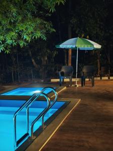 a swimming pool with an umbrella and chairs and a table at Villa Mountain Pearl in Chikmagalūr +2 photos