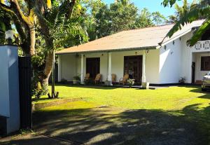 a white house with chairs in a yard at Villa Mango Serenity in Hikkaduwa
