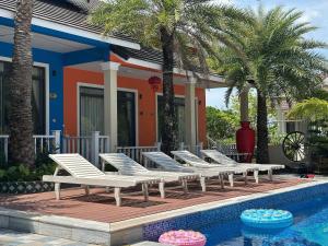 a row of white lounge chairs next to a swimming pool at The Palm Phu Quoc Resort & Villa in Phú Quốc