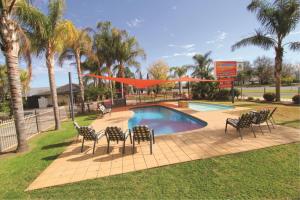 a group of chairs around a swimming pool with palm trees at All Seasons Mildura Holiday Park in Mildura