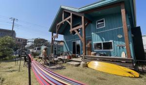 a man standing in front of a house with a surfboard at B&BHOUSE FAM in Ichinomiya