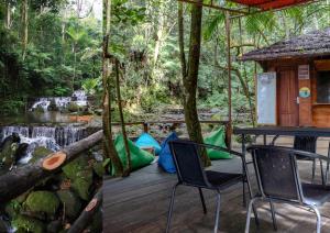 a deck with chairs and a table and a waterfall at Glamping Camphills in Gunungpicung