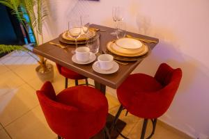 a dining table with red chairs and plates and glasses at Suite Kimia - Chic T2, Rue Des Jardins, Cocody, Vallon, Abidjan in Abidjan