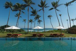a swimming pool with chairs and umbrellas and the ocean at Cape Weligama - Relais and Chateaux in Weligama