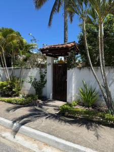 a gate to a house with a fence and palm trees at Suite LUAR in Saquarema