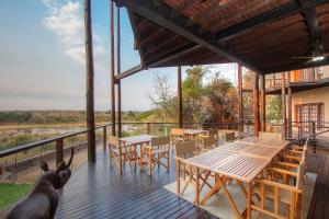 a deck with tables and chairs and a view of a river at Kruger Private Lodge in Marloth Park