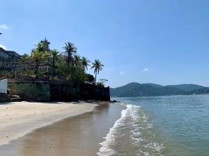a beach with a house and palm trees and the water at Casa de praia em Itacuruçá in Mangaratiba