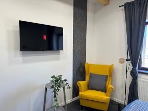 a yellow chair and a television on a wall at Házikon 2 Apartman in Igricetanya