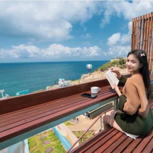 a girl sitting on a balcony reading a book at HeHa Ocean Glamping dan Cabin in Ngundel +7 photos