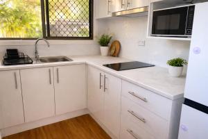 a kitchen with white cabinets and a sink and a microwave at Hidden Gem at The Bay - Resort Pool - 300m to Beach in Urangan