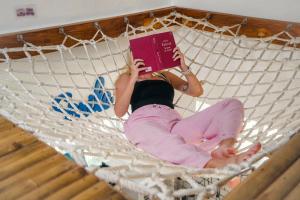 a girl laying in a hammock reading a book at L'Astrolabe - Ocean View Tiny House in Baras
