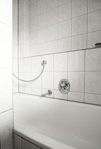 a white tiled bathroom with a shower with a hose at Ferienwohnungen Steinbacher in Vogtareuth