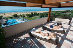 two people laying on beds on a balcony with a pool at Savoy Beach Hotel & Thermal Spa in Bibione