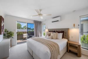 a white bedroom with a bed and a balcony at Mooloolaba Canal Retreat with Pool Sleeps 12 in Mooloolaba